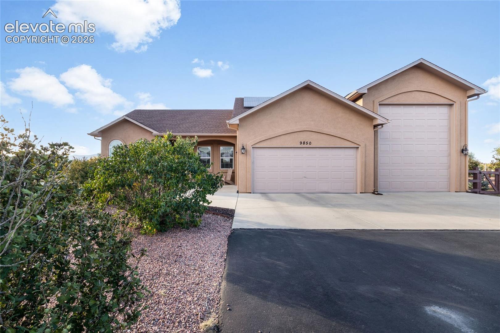 Stucco exterior featuring a two-car garage, an additional high-clearance RV bay, concrete driveway, and roof-mounted solar panels