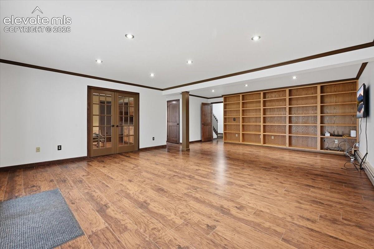 Spacious room featuring wood-finish flooring, recessed lighting, built-in shelving, and French doors