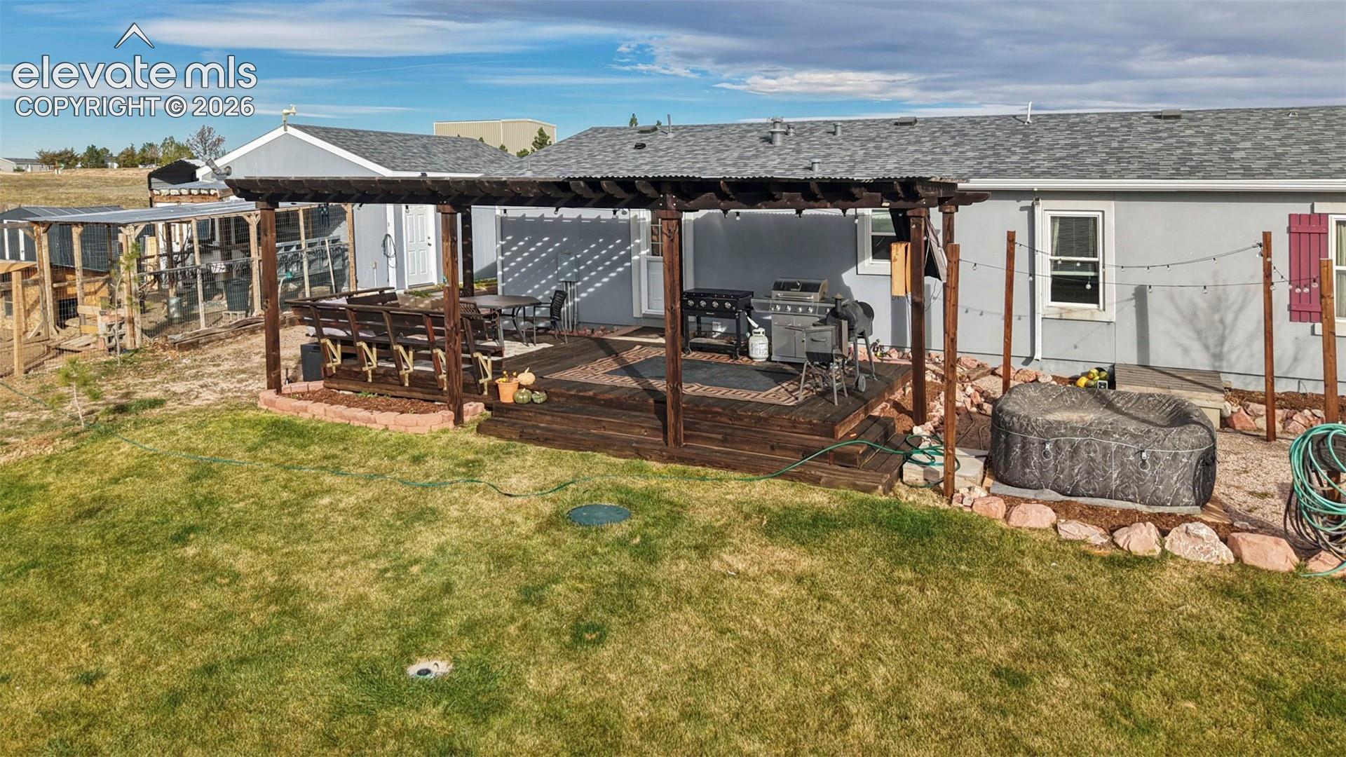 Multi-level dark wood deck with an attached overhead pergola, integrated rock-border landscaping, and a manicured lawn