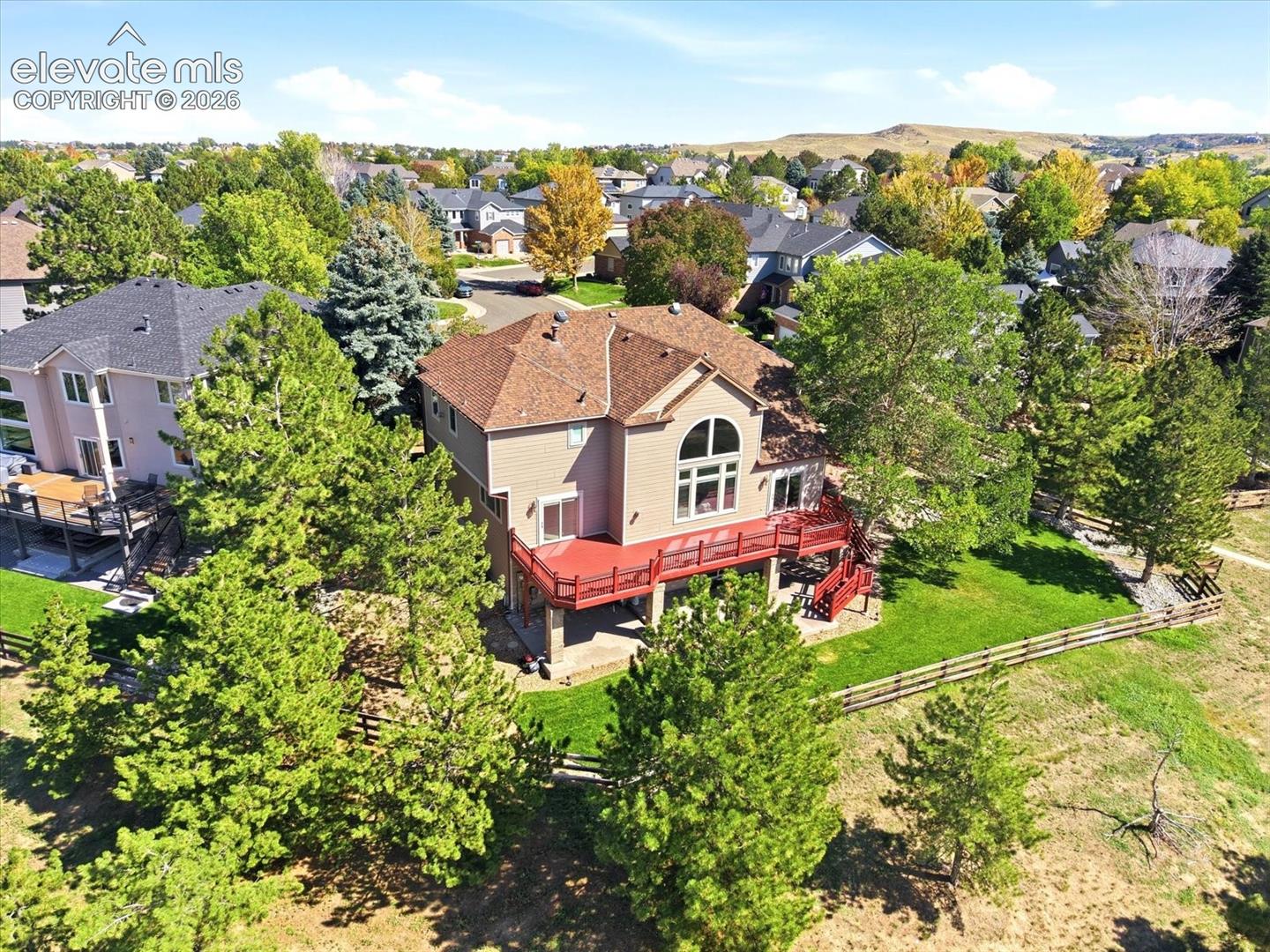 Two-story residence featuring an elevated deck, ground-level patio, expansive rear lawn, and mature evergreen trees