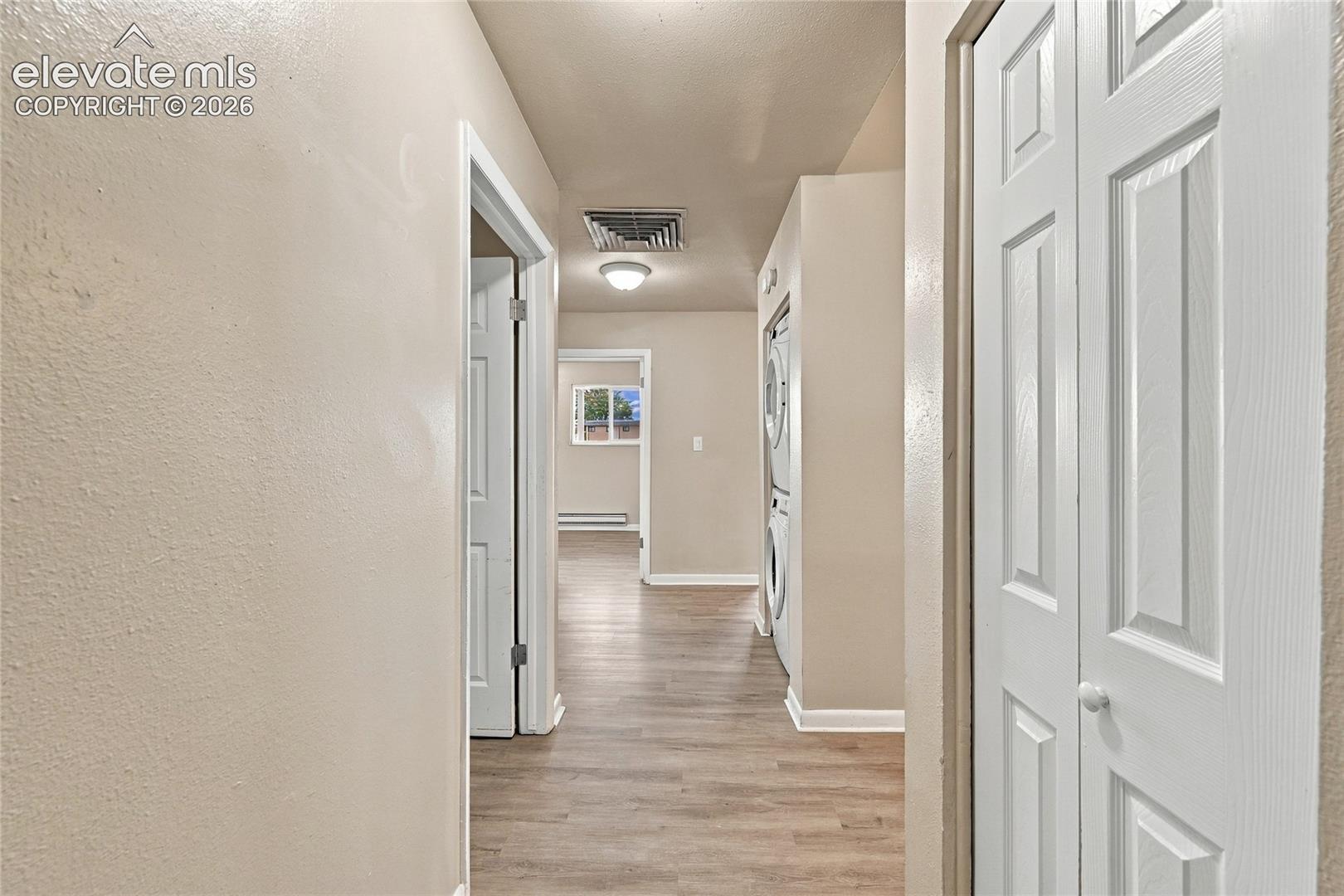 Hallway featuring wood-finish flooring, two-panel interior doors, recessed ceiling lighting, and a built-in laundry closet with stacked appliance capability