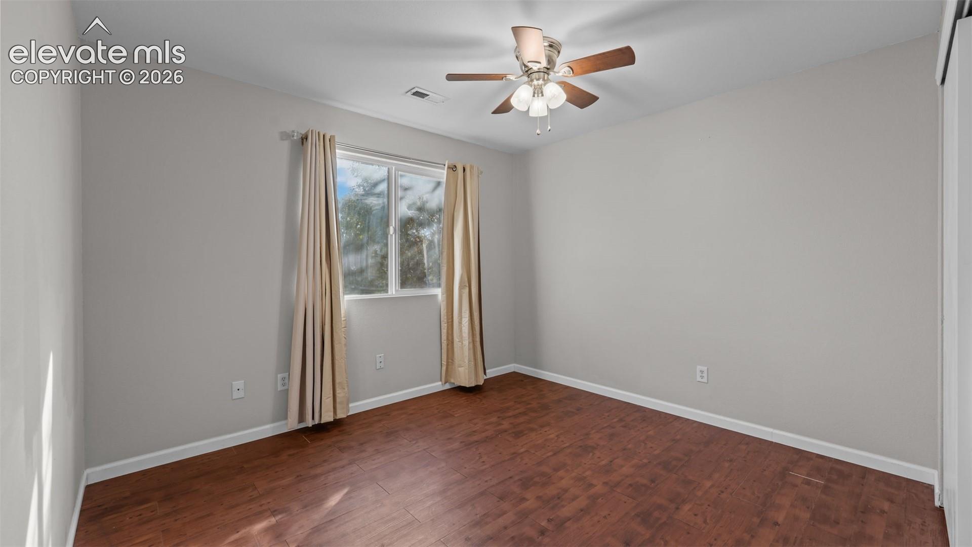 Wood-finish flooring, a ceiling fan with integrated lighting, and a window providing natural illumination