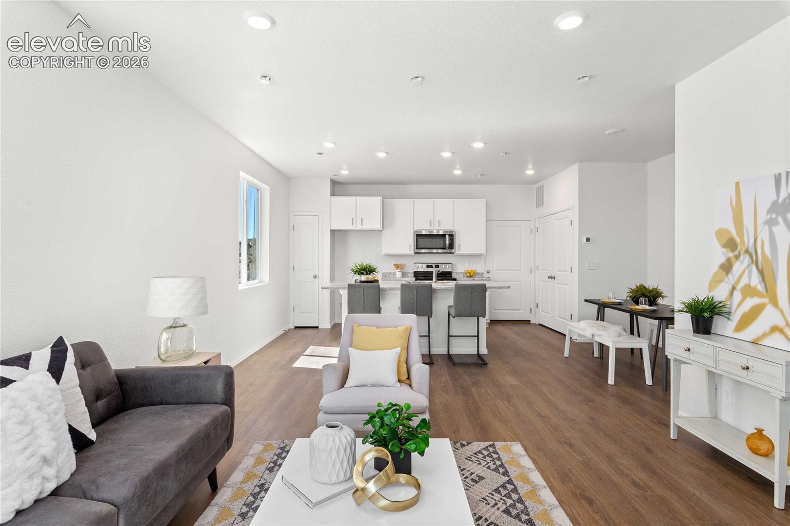 Open-concept living space featuring wood-finish flooring, recessed lighting, and a kitchen with white cabinetry and stainless steel appliances
*photos  of a model home*