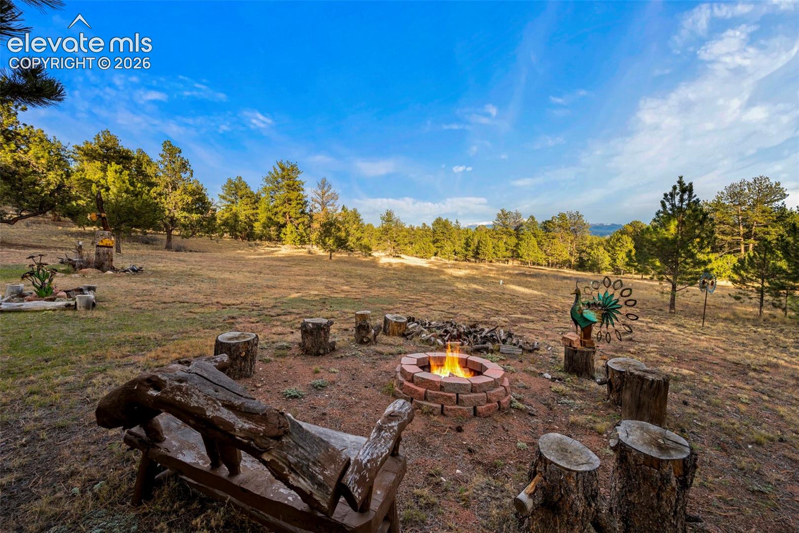 Circular stone-block fire pit situated on a natural landscape with mature pine trees and expansive grounds
