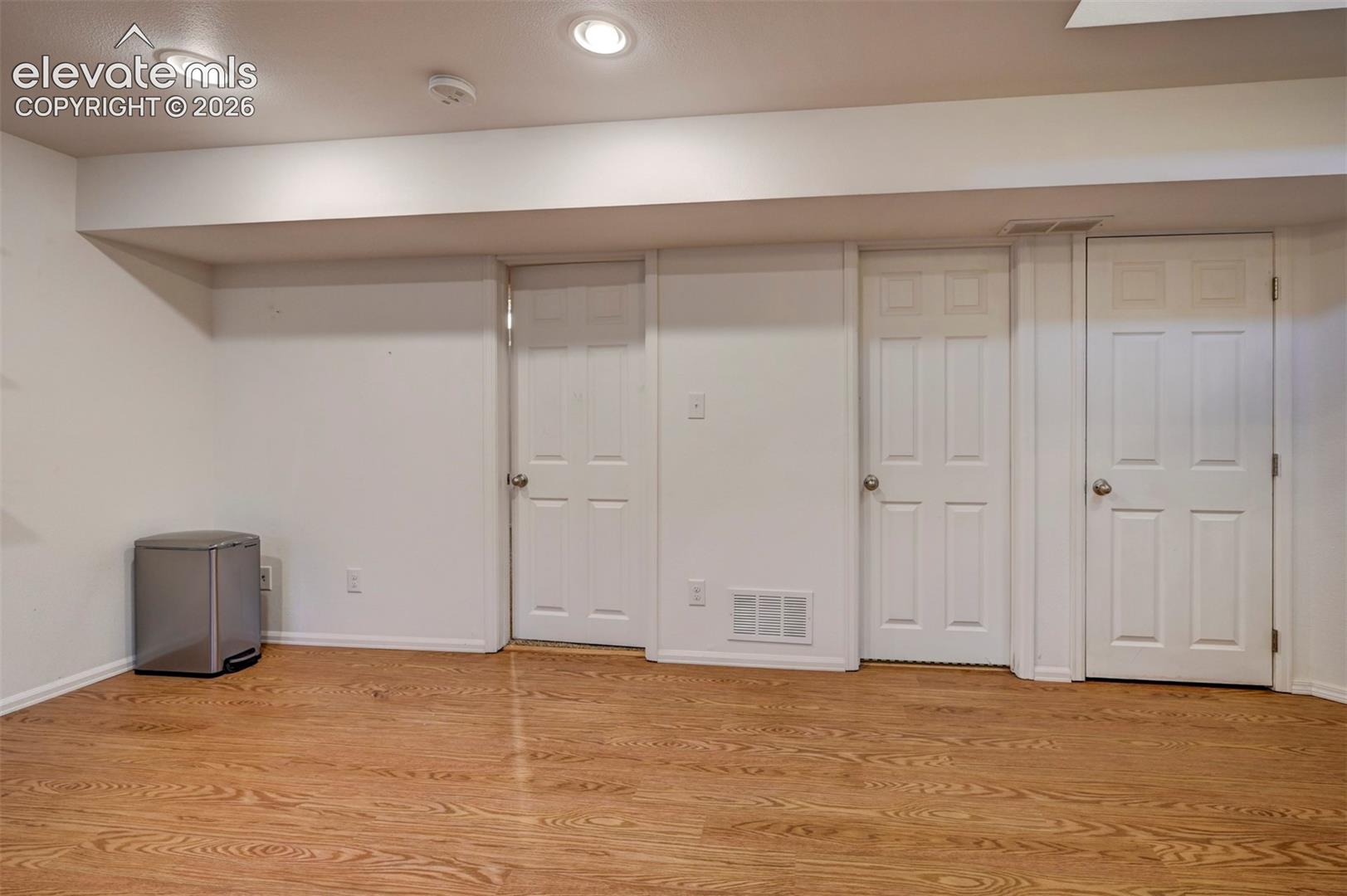 Wood-finish flooring with recessed lighting, multiple paneled doors, and white walls