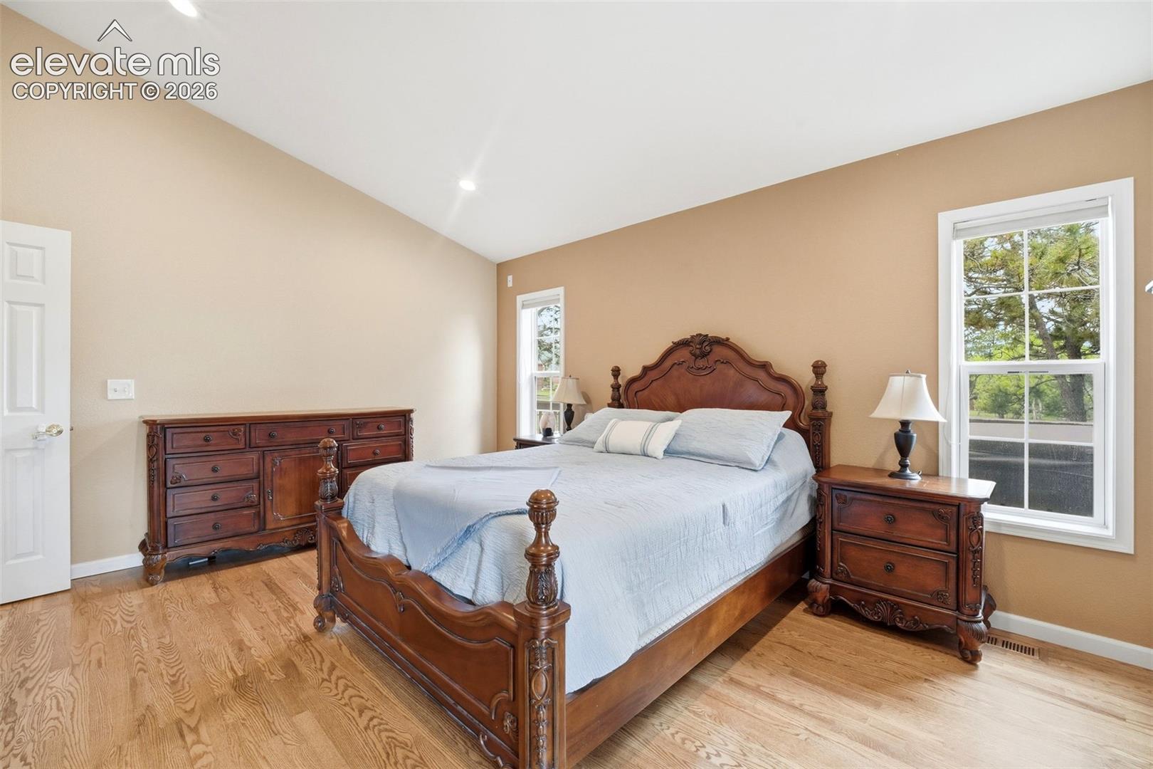 Vaulted ceiling room featuring light wood-finish flooring, recessed lighting, and two windows with white trim