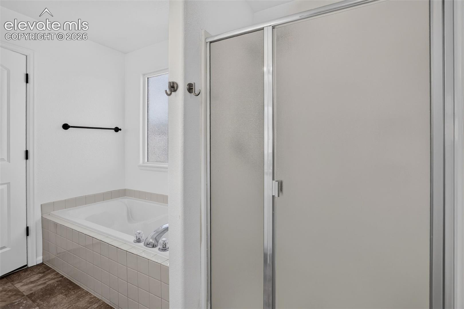 Built-in soaking tub with tile surround, frosted glass shower enclosure, and a small window