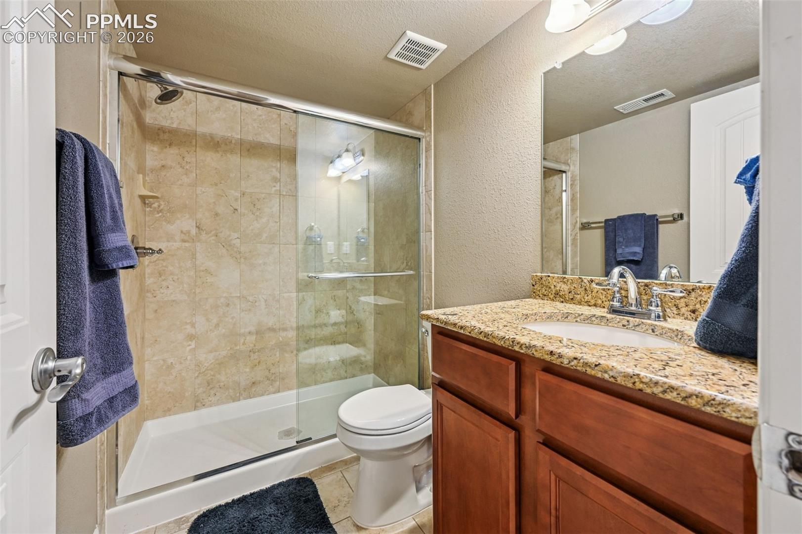 Bathroom with a textured ceiling, a textured wall, vanity, a shower stall, and light tile patterned floors