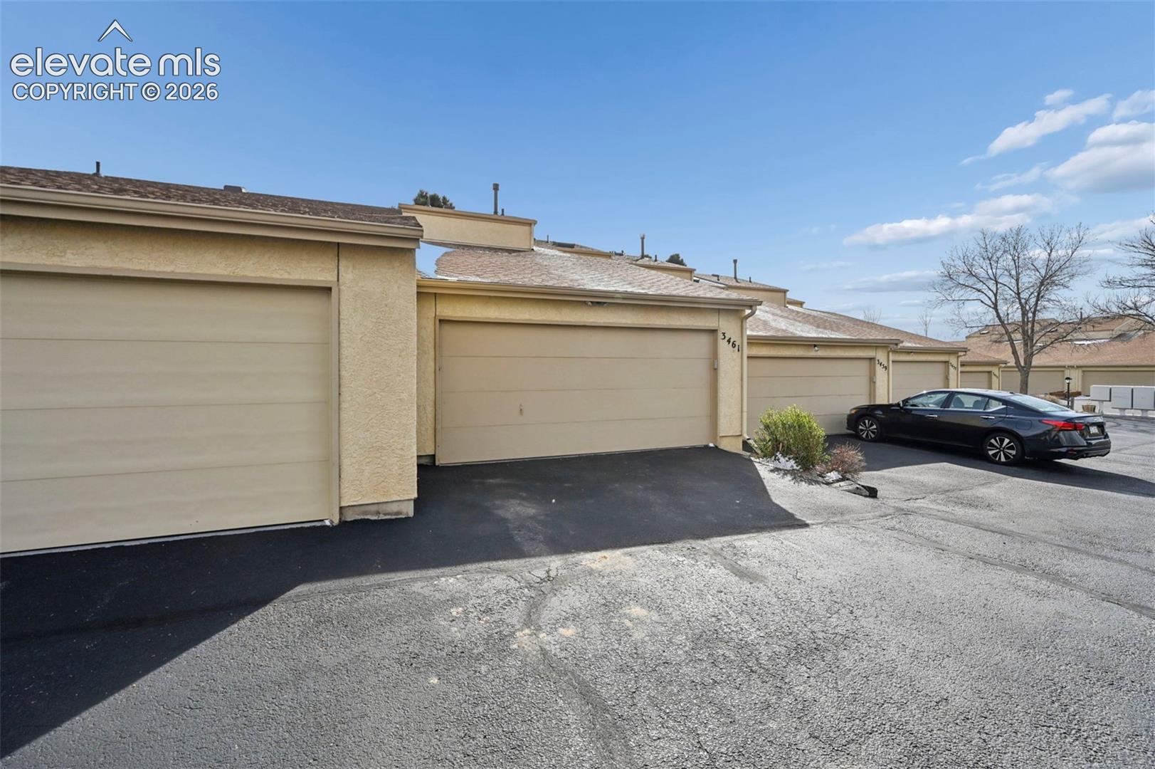 Stucco exterior with multiple attached garages, featuring asphalt driveways and a pitched roofline