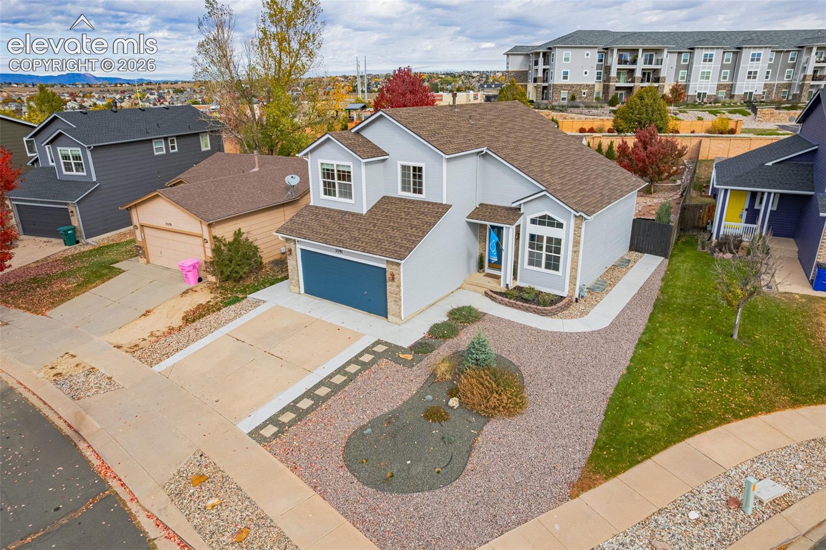 Two-story residence featuring a multi-textured exterior of siding and stone veneer, shingled roof, attached two-car garage, and xeriscaped front yard with decorative stone pathways