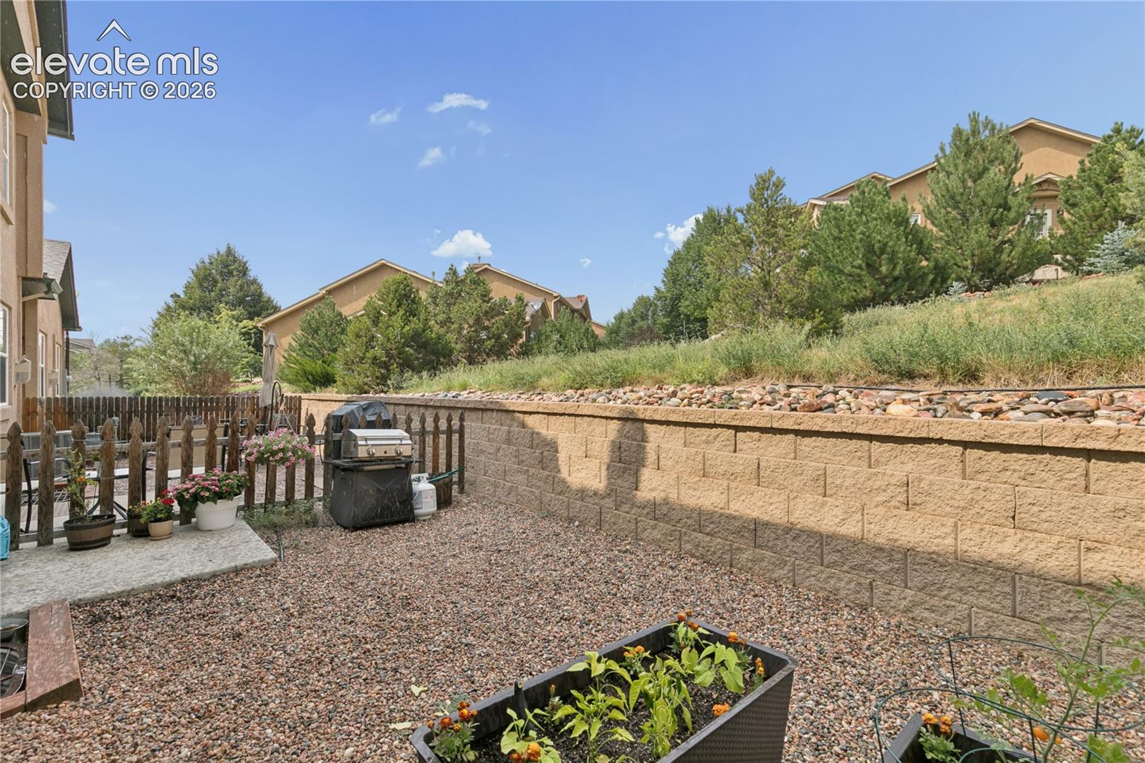 Private backyard featuring a stone retaining wall, gravel ground cover, and a picket fence