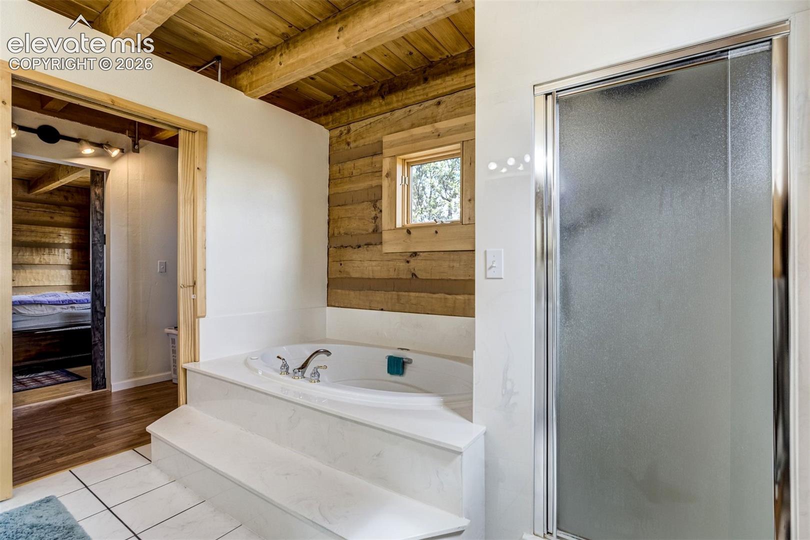 Soaking tub with built-in steps, adjacent to a frosted glass shower enclosure