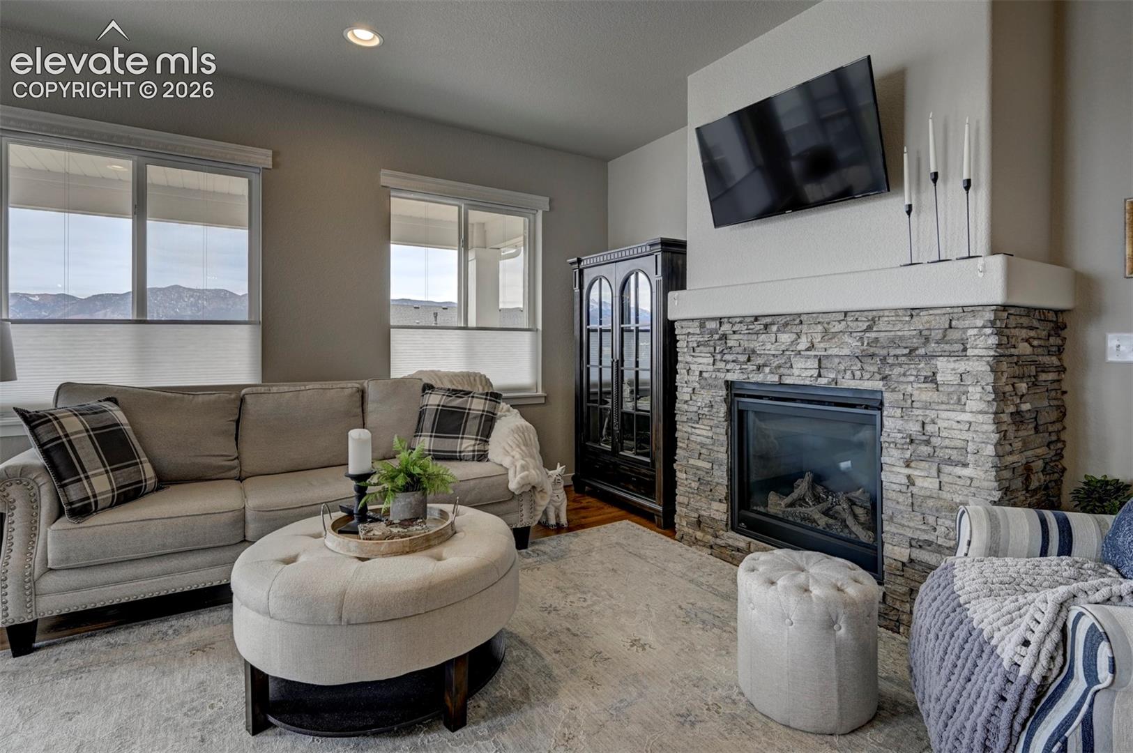 Living area featuring a stacked stone fireplace with a raised hearth, recessed lighting, and expansive windows