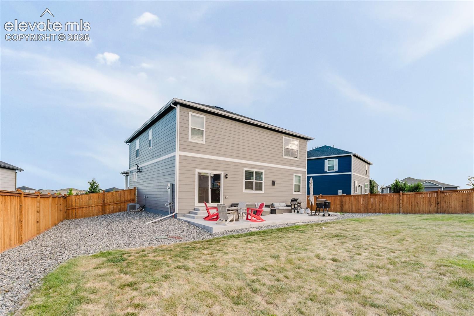 Fenced backyard with auto sprinklers, grassy area, rock beds, and a concrete patio for outdoor dining and relaxation.