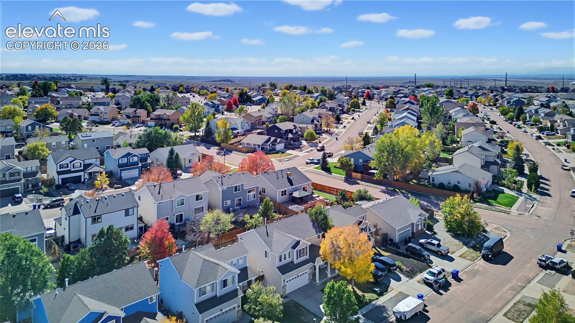 Aerial perspective of a residential neighborhood featuring multi-story dwellings, paved roadways, mature deciduous trees, and expansive horizon scenery