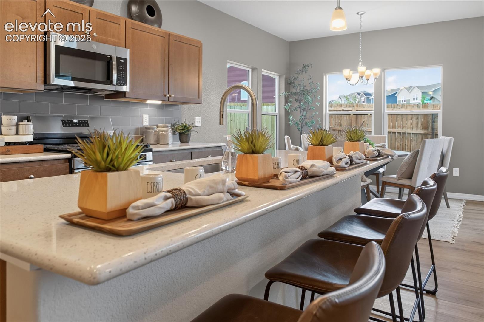 Kitchen featuring wood-finish cabinetry, neutral solid-surface countertops, a subway tile backsplash, built-in microwave, and wood-finish flooring