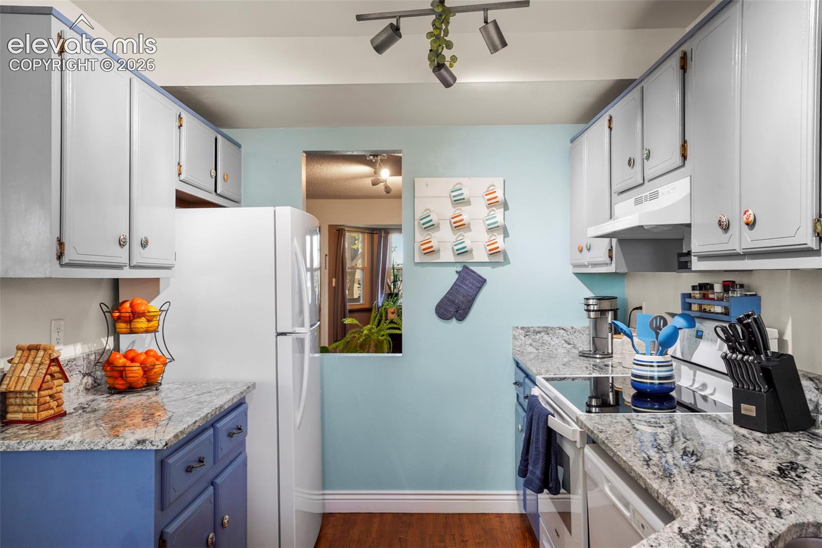 Kitchen featuring natural stone countertops, custom cabinetry, wood-finish flooring, and track lighting