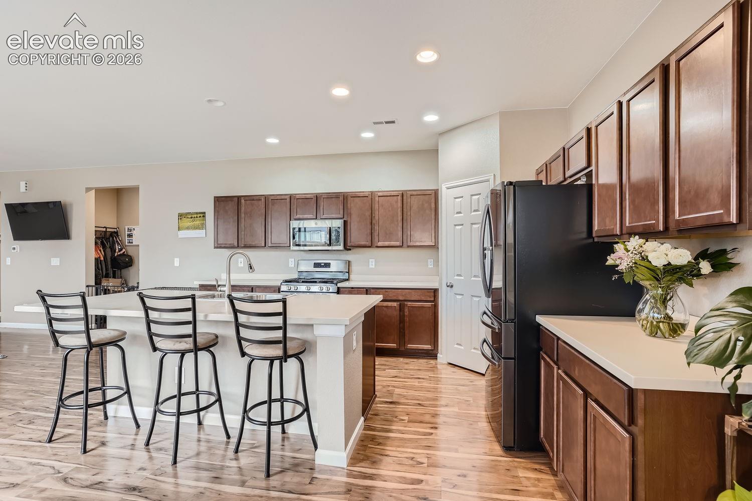 Kitchen featuring stained wood cabinetry, quartz countertops, central island with integrated seating, stainless steel appliances, and wood-finish flooring