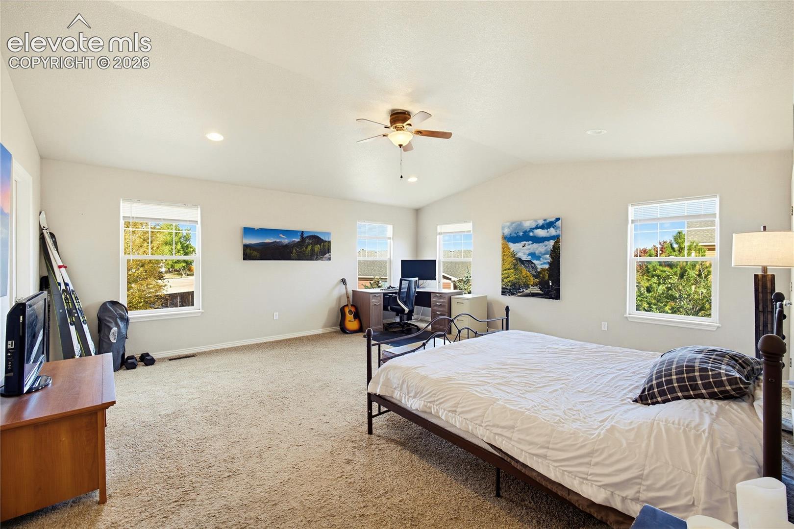 Spacious room featuring a vaulted ceiling, recessed lighting, a central ceiling fan, and large windows