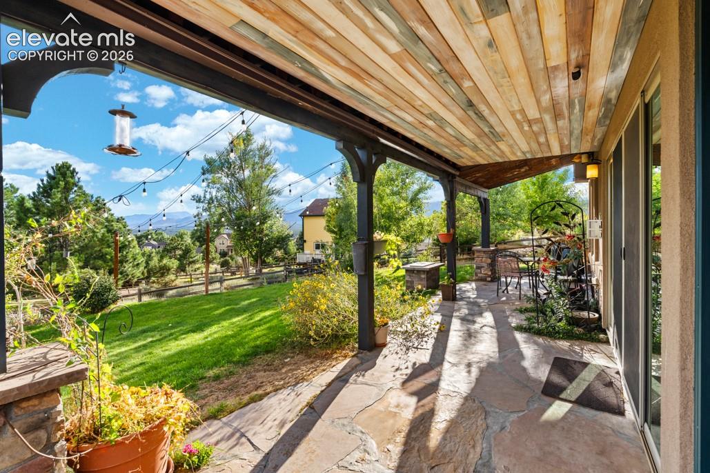 Covered patio with a wood-plank ceiling, flagstone flooring, and stone-clad support columns