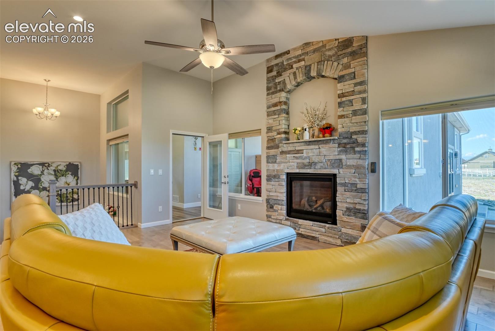 Vaulted ceiling with a ceiling fan, gas-log fireplace, wood-finish flooring, recessed lighting, and multiple windows.