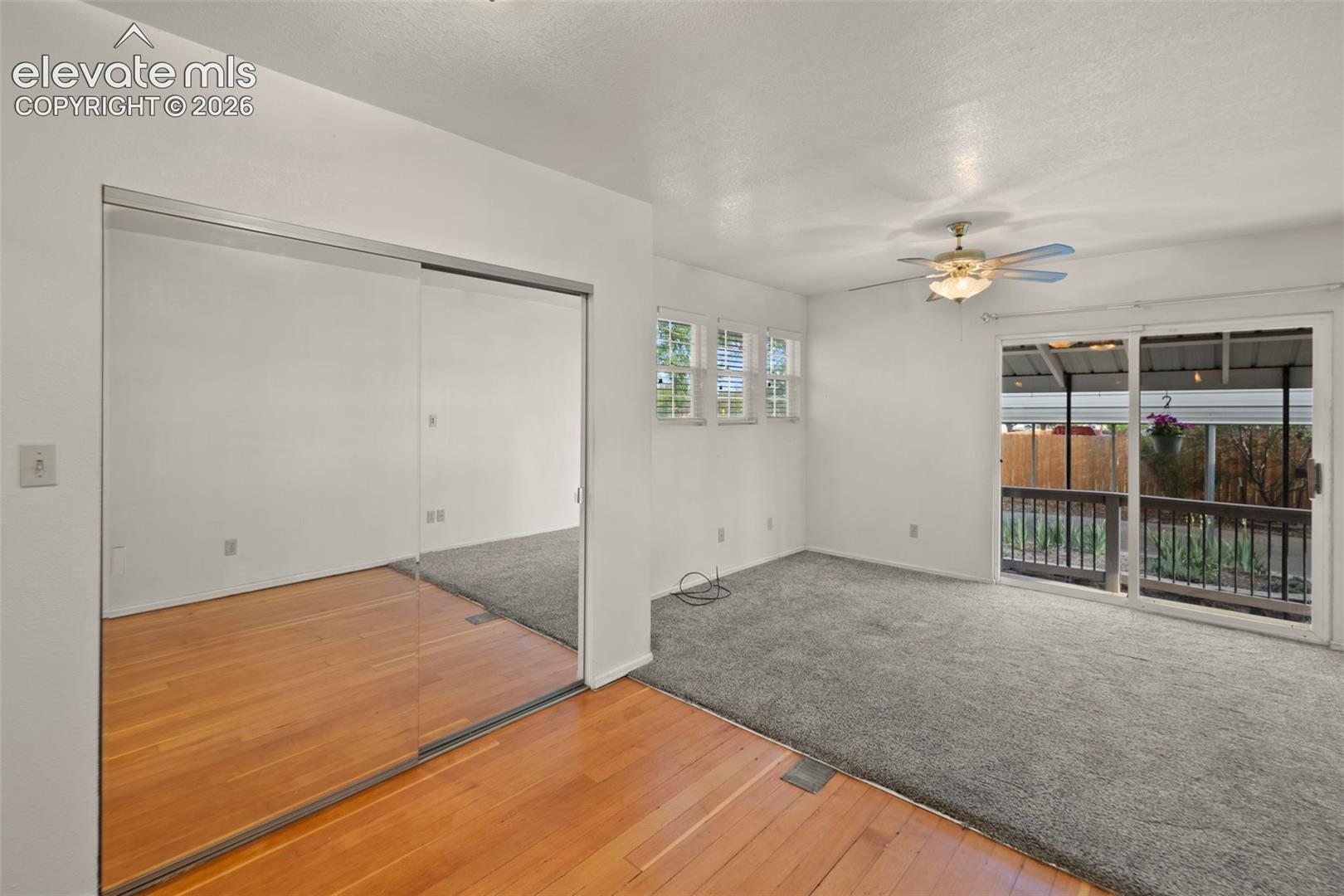 Mirrored sliding closet doors, wood-finish flooring, carpeted area, multi-pane windows, and a ceiling fan with light fixture