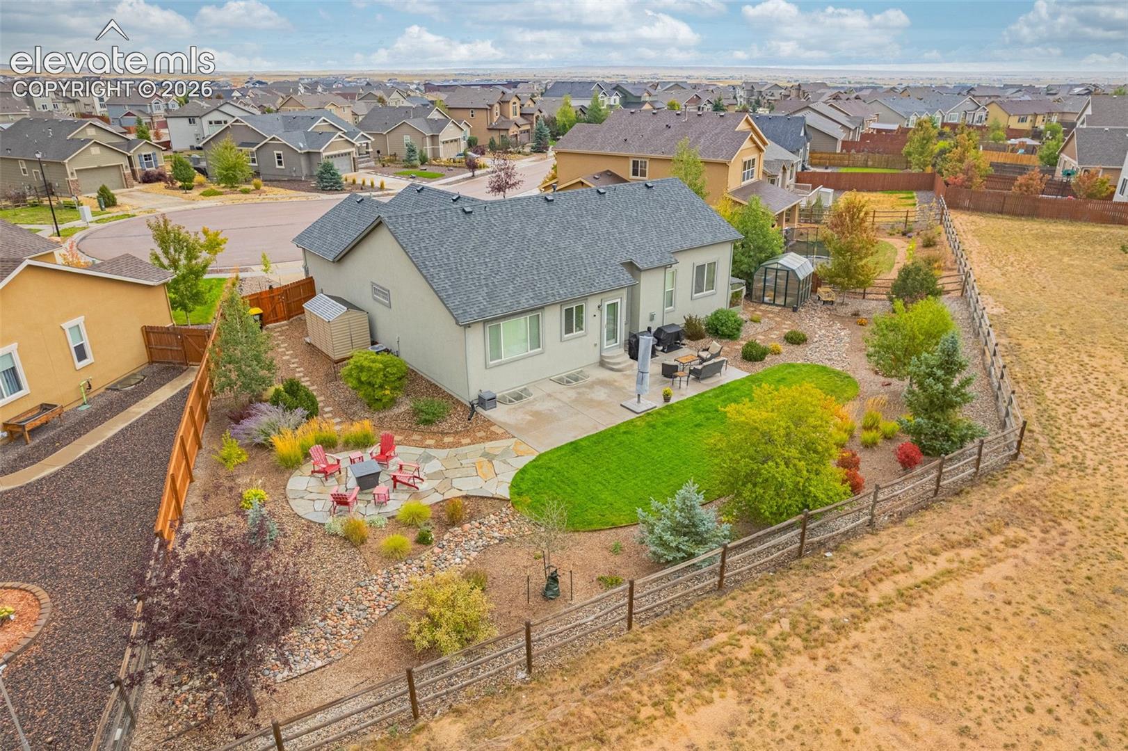 Rear exterior featuring a concrete patio, stone paver seating area, manicured lawn, mixed ornamental landscaping, and wood perimeter fencing