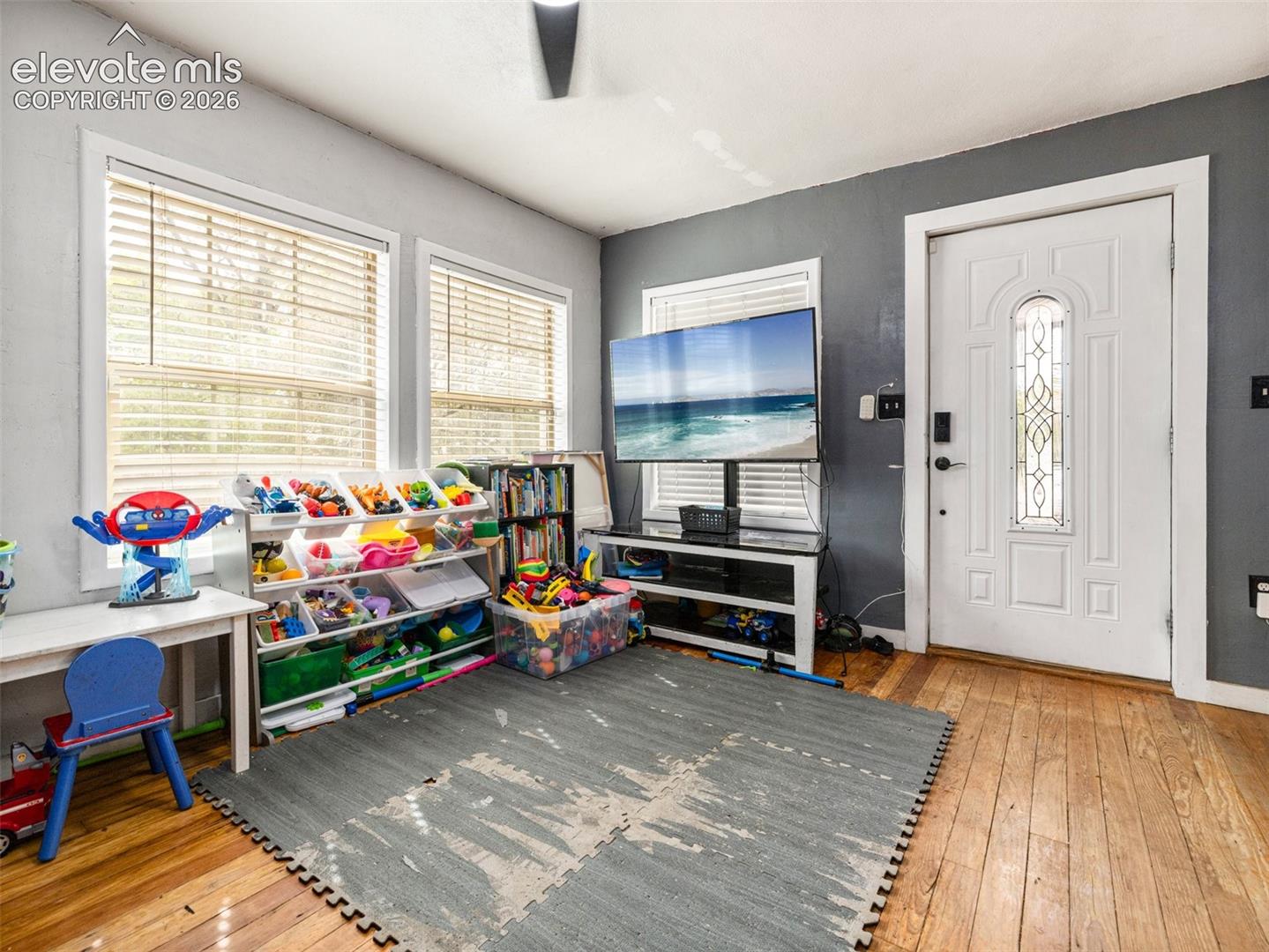 Hardwood flooring, multiple windows with blinds, and a white paneled door with decorative glass inlay