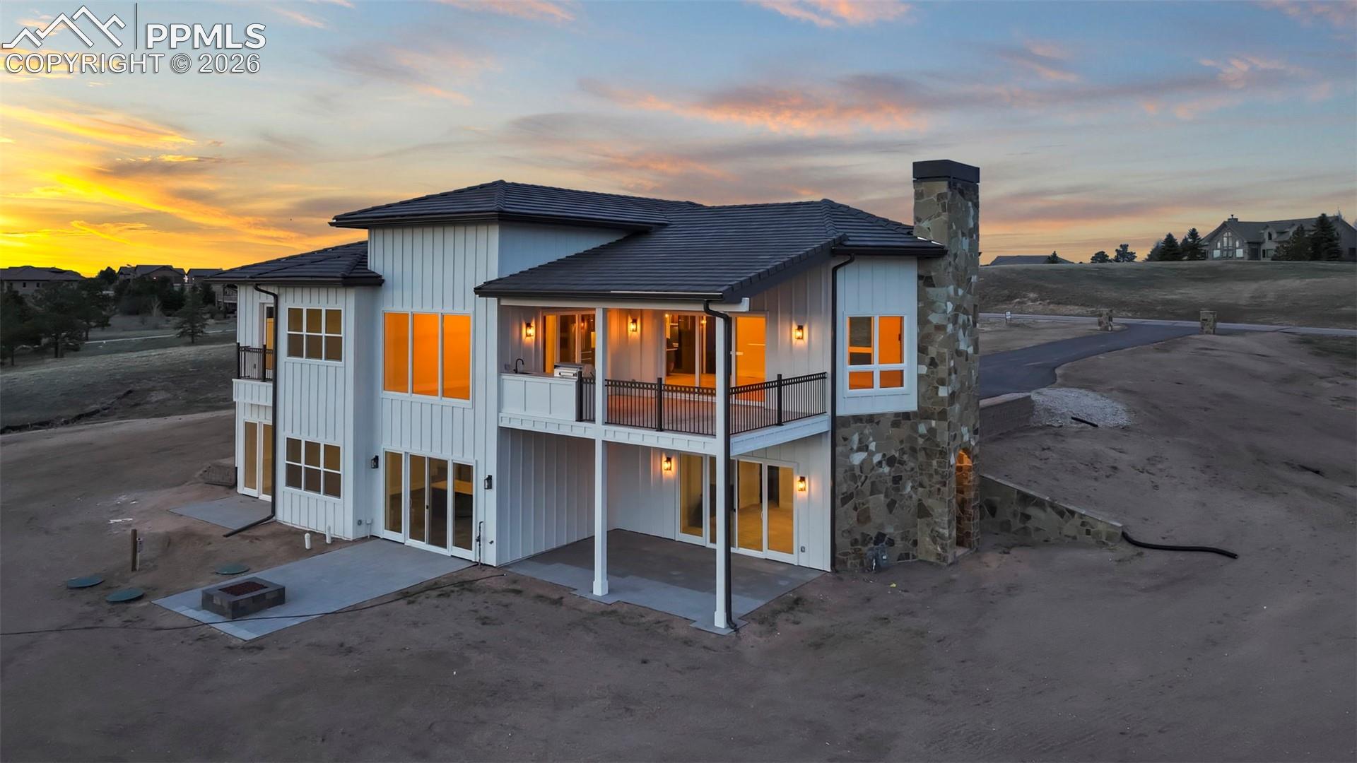 Back of property at dusk featuring a patio, board and batten siding, a chimney, and a balcony