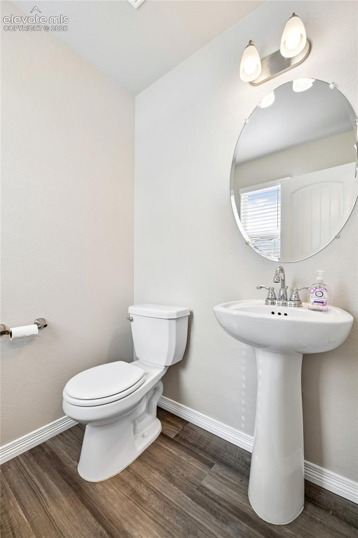 Powder room featuring wood-finish flooring, a white pedestal sink with a polished chrome faucet, an oval wall-mounted mirror, and a two-light vanity fixture