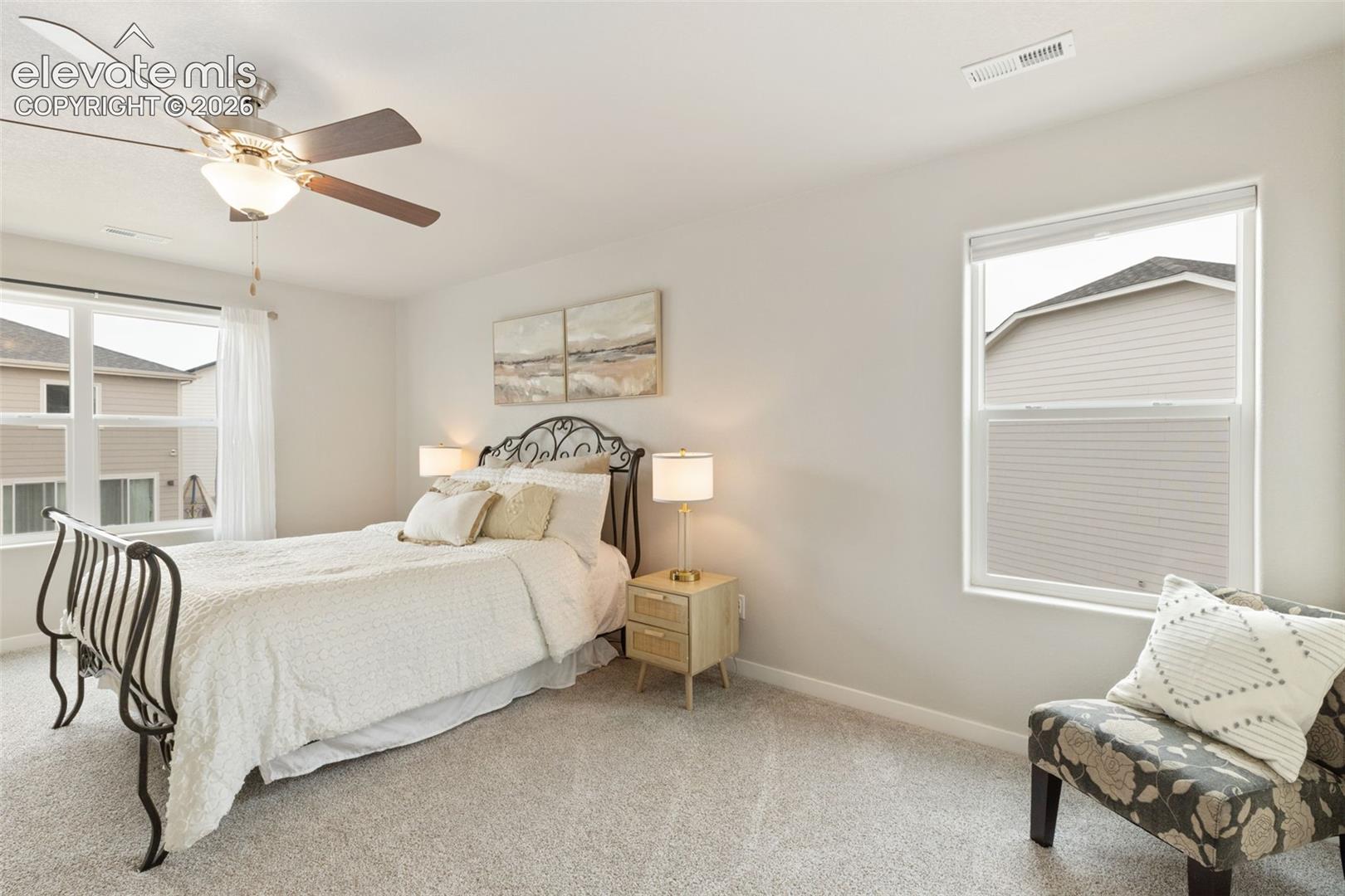 Bedroom featuring neutral wall paint, light gray carpeting, a multi-blade ceiling fan with integrated lighting, and two windows with white trim