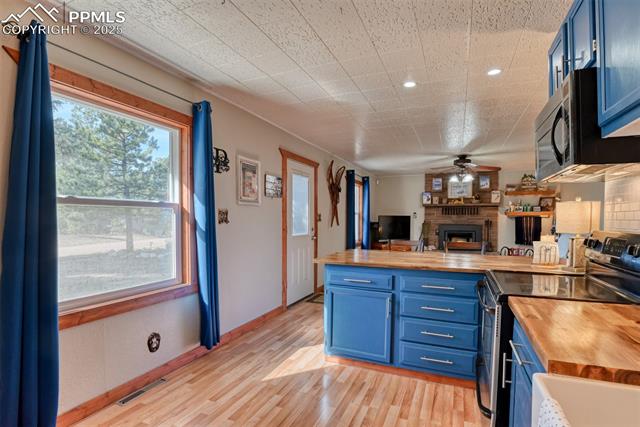 Kitchen featuring blue cabinetry, stainless steel electric range oven, wooden counters, a peninsula, and light wood-style floors