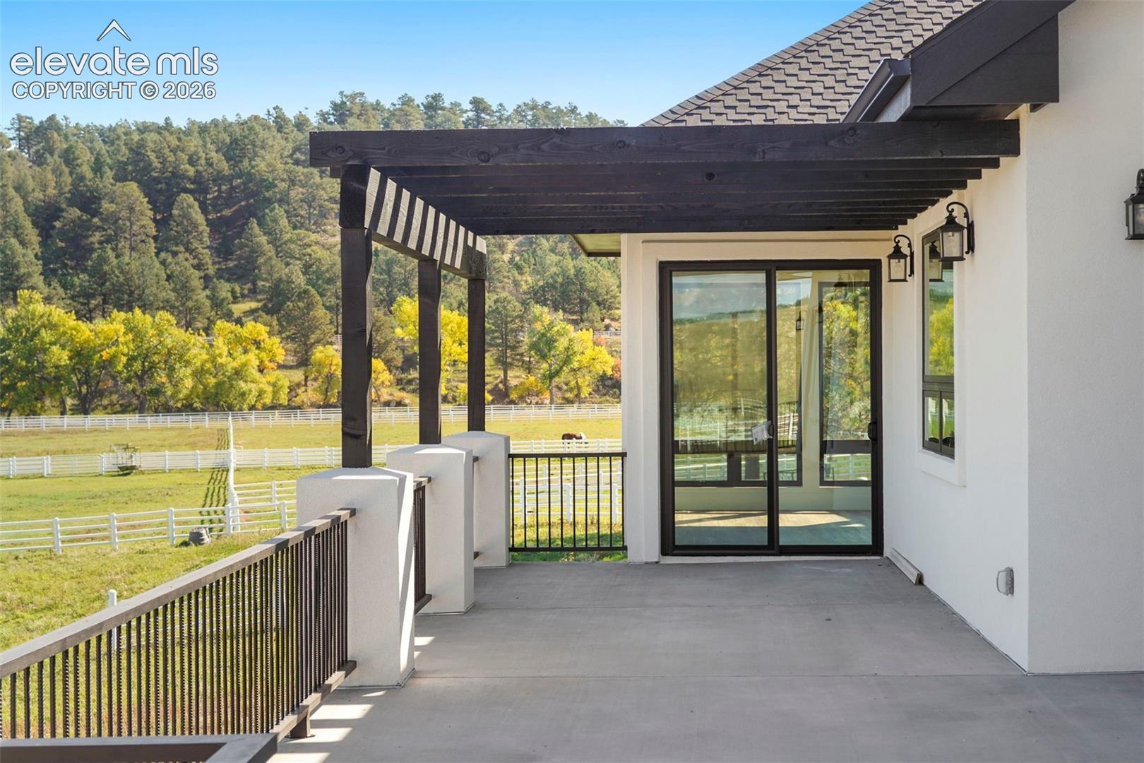 Spacious outdoor patio with dark wood pergola, black metal railings, and dual exterior sconces