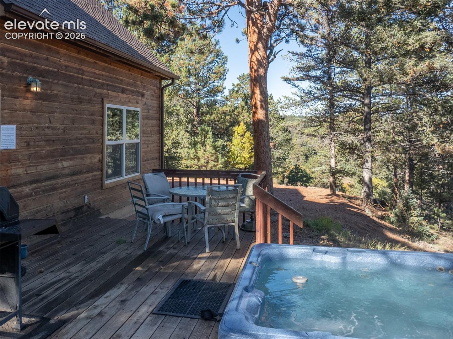 Expansive wooden deck with a built-in hot tub, offering abundant natural light and a surrounding natural landscape