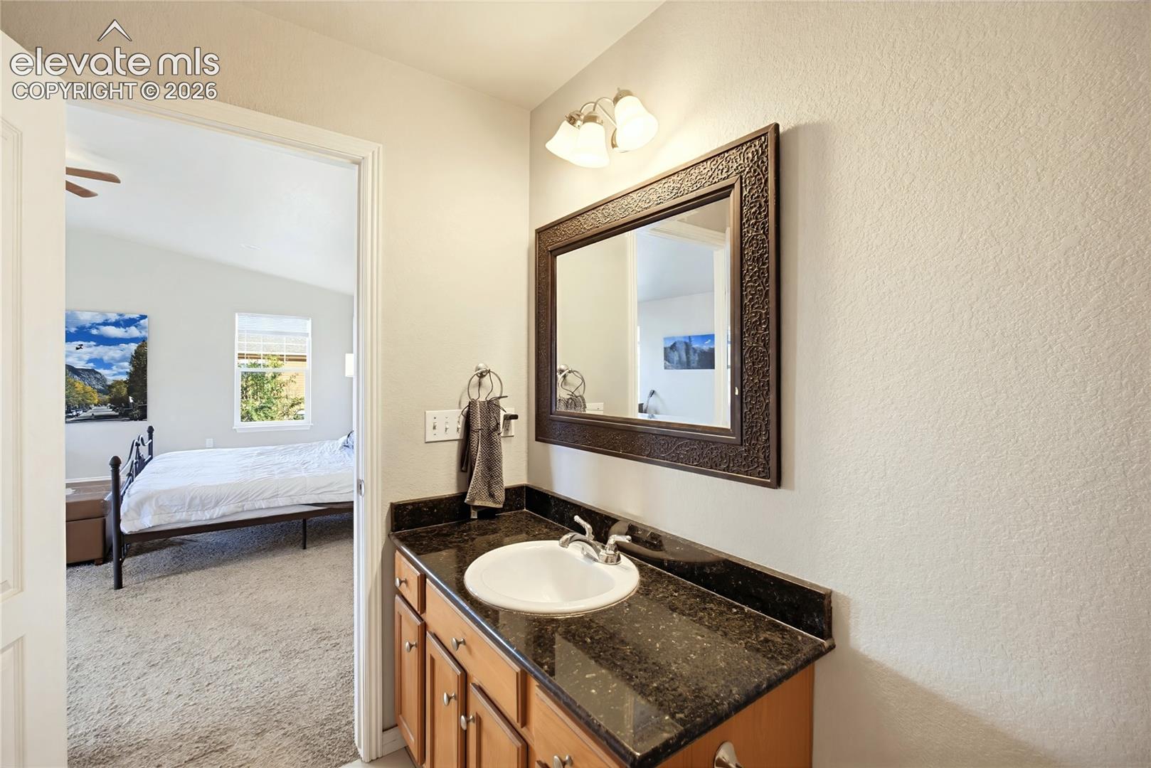 Vanity featuring a dark stone countertop, an integrated white oval basin, wood-finish cabinetry, a framed wall mirror, and a multi-bulb light fixture
