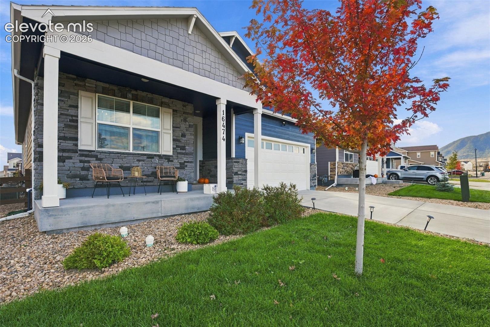 Single-story exterior featuring stone veneer accents, shake siding, a covered front porch, and a multi-panel garage door