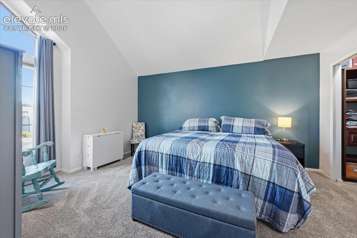 Vaulted ceilings, neutral carpeting, accent wall, and large window