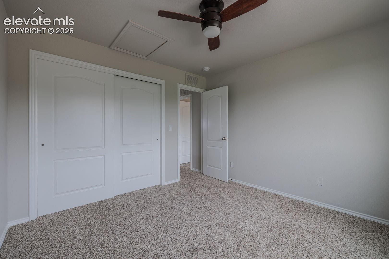 Spacious bedroom featuring neutral wall finishes, plush carpeting throughout, a ceiling fan with integrated lighting, and dual closets with white six-panel doors providing ample storage solutions