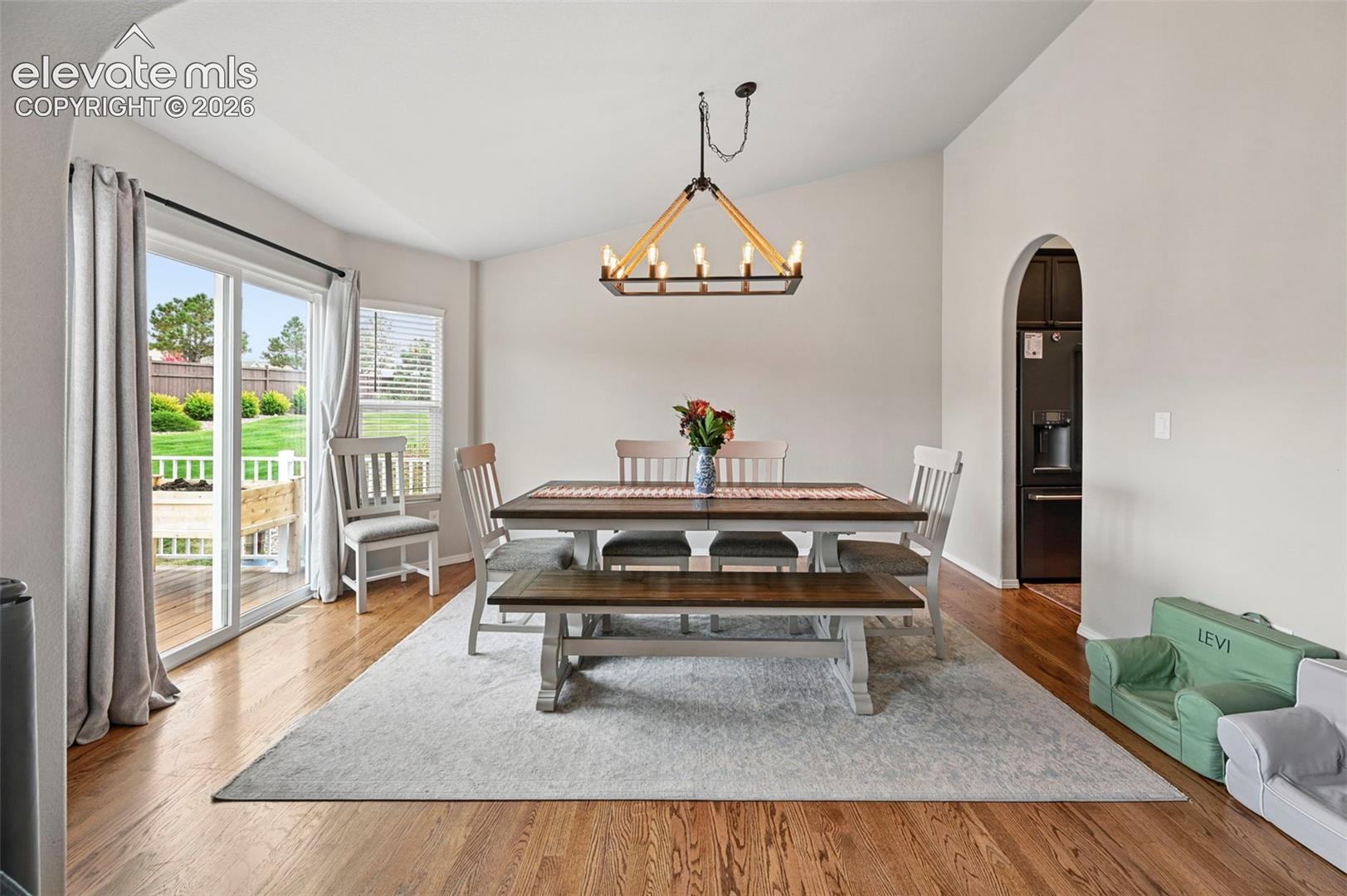 Dining area featuring vaulted ceilings, wood-finish flooring, a multi-light chandelier with metallic accents, arched entryway, and a sliding glass door