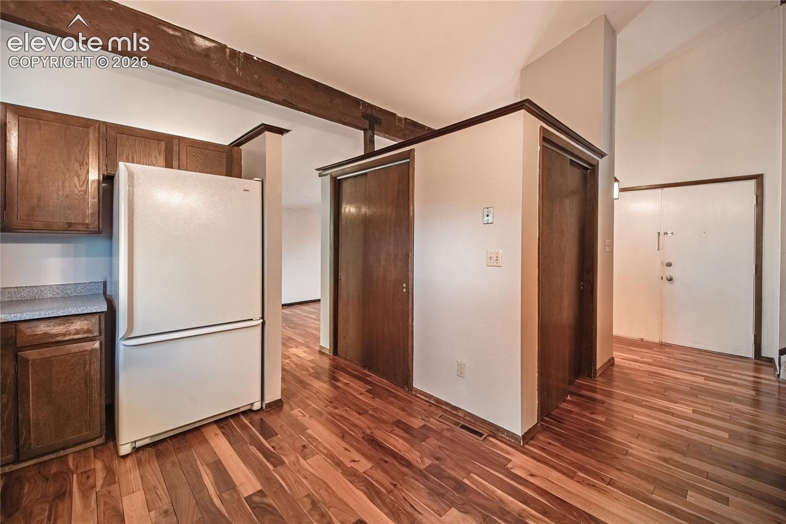 Vaulted ceilings featuring exposed timber beams, wood-finish flooring, and recessed cabinetry with stone-finish countertops