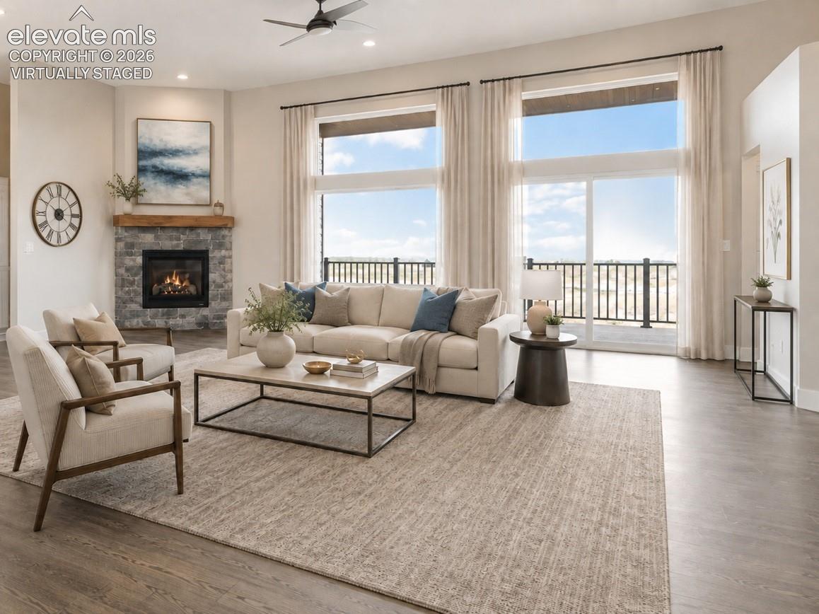 Virtually Staged Spacious living area featuring expansive windows with sliding glass doors, a corner stone fireplace with a substantial wood mantel, a ceiling fan with integrated lighting, recessed lighting, and wood-finish flooring