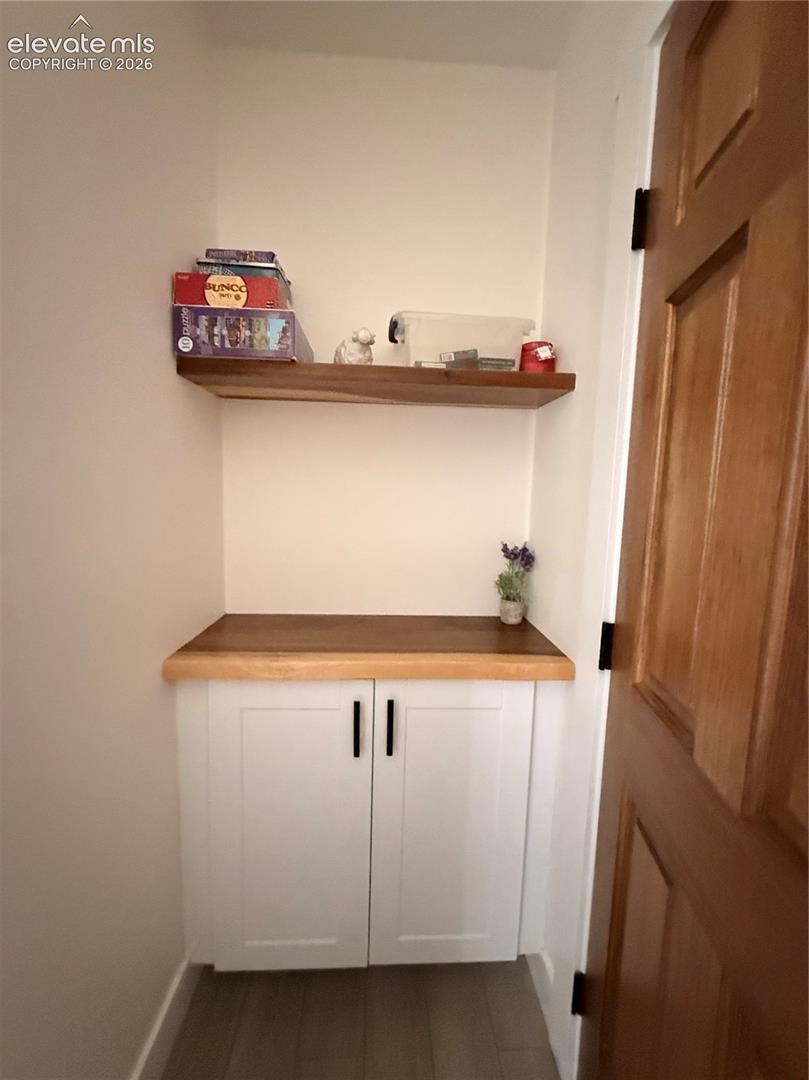 Built-in cabinetry with white shaker-style doors, wood-finish countertop, and a floating wood-finish shelf