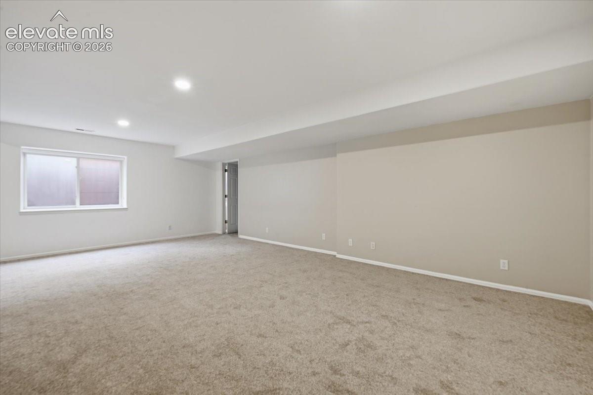 Neutral-toned interior space featuring neutral carpeting, recessed ceiling lighting, and a window with a horizontal slider