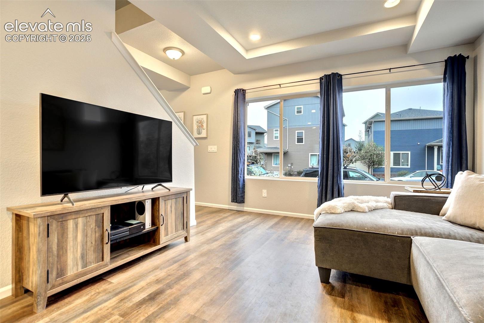 Tray ceiling with recessed lighting, large picture windows, and wood-finish flooring