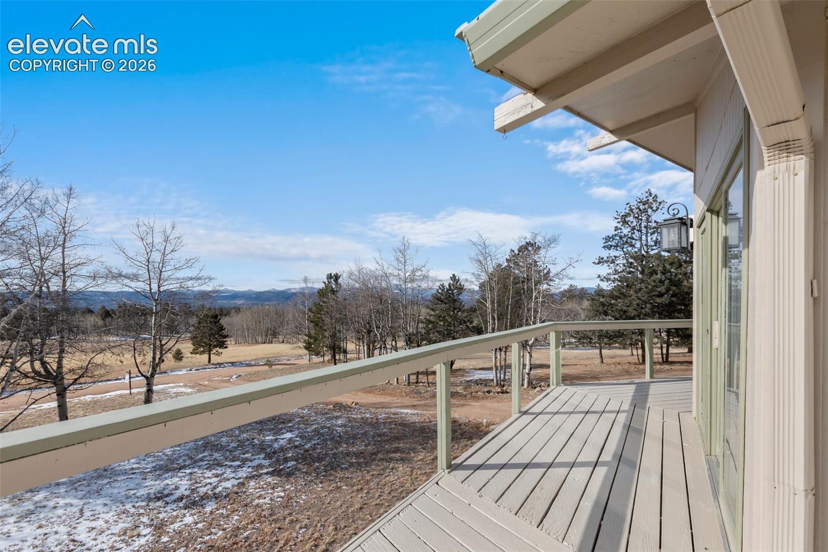 Expansive outdoor deck with wood-finish decking and railing, offering open sky and distant natural scenery