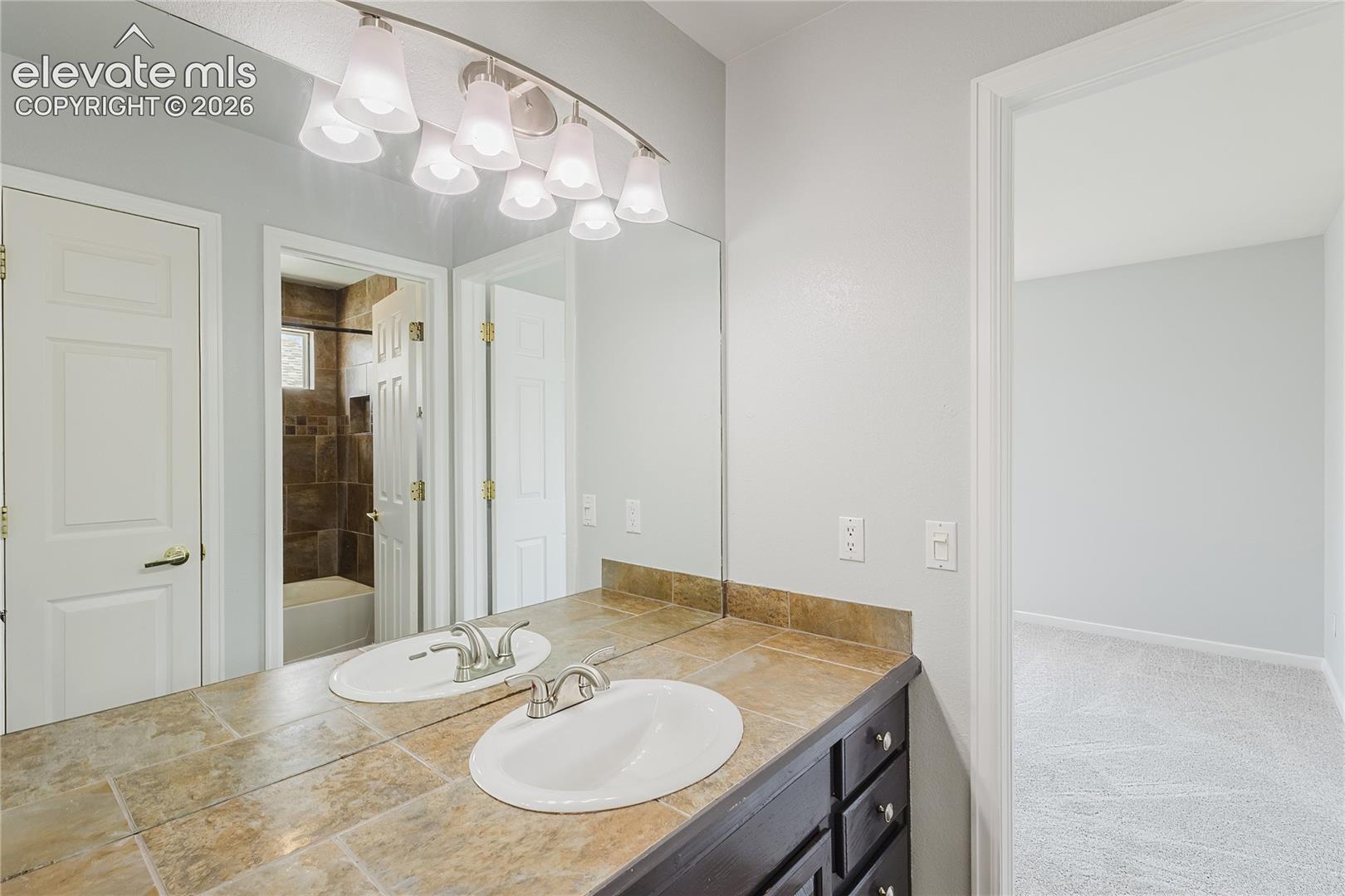Dual vanity with integrated sinks, tiled countertop, and track lighting