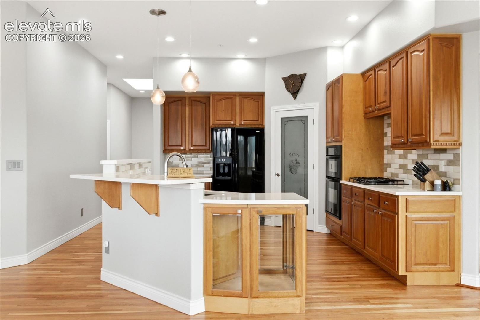 Kitchen featuring wood cabinetry, light-toned countertops, a tile backsplash, and wood-finish flooring