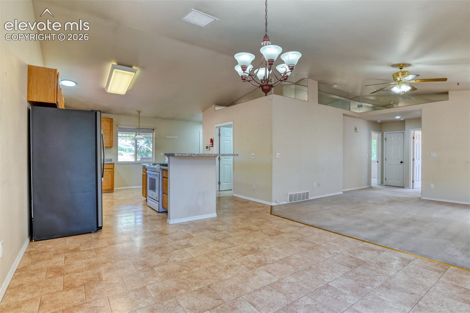 Kitchen featuring stone-finish countertops, natural wood cabinetry, a decorative multi-arm chandelier, tiled flooring, and a ceiling fan