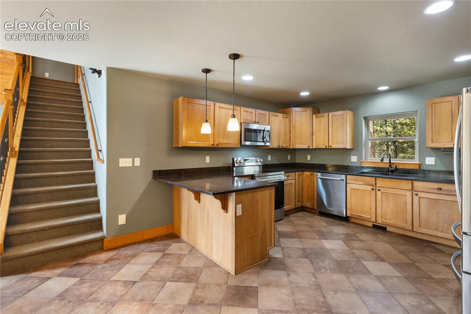 Kitchen featuring natural wood cabinetry, stone-surface countertops, stainless steel appliances, dual pendant lighting, and tile flooring