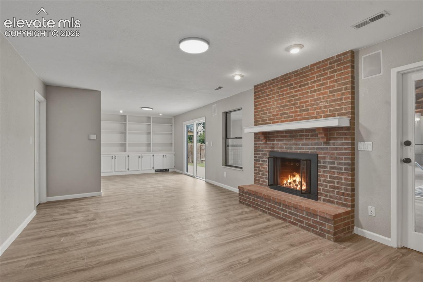 Brick-clad fireplace with a hearth, built-in shelving, wood-finish flooring, and glass sliding doors